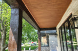 Wood ceiling panels installed on a covered porch, shown alongside dark wooden posts, a stone wall, black-framed windows, and outdoor greenery.